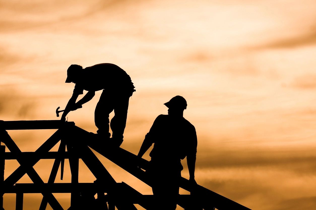 Two men working on a wooden structure at sunset.