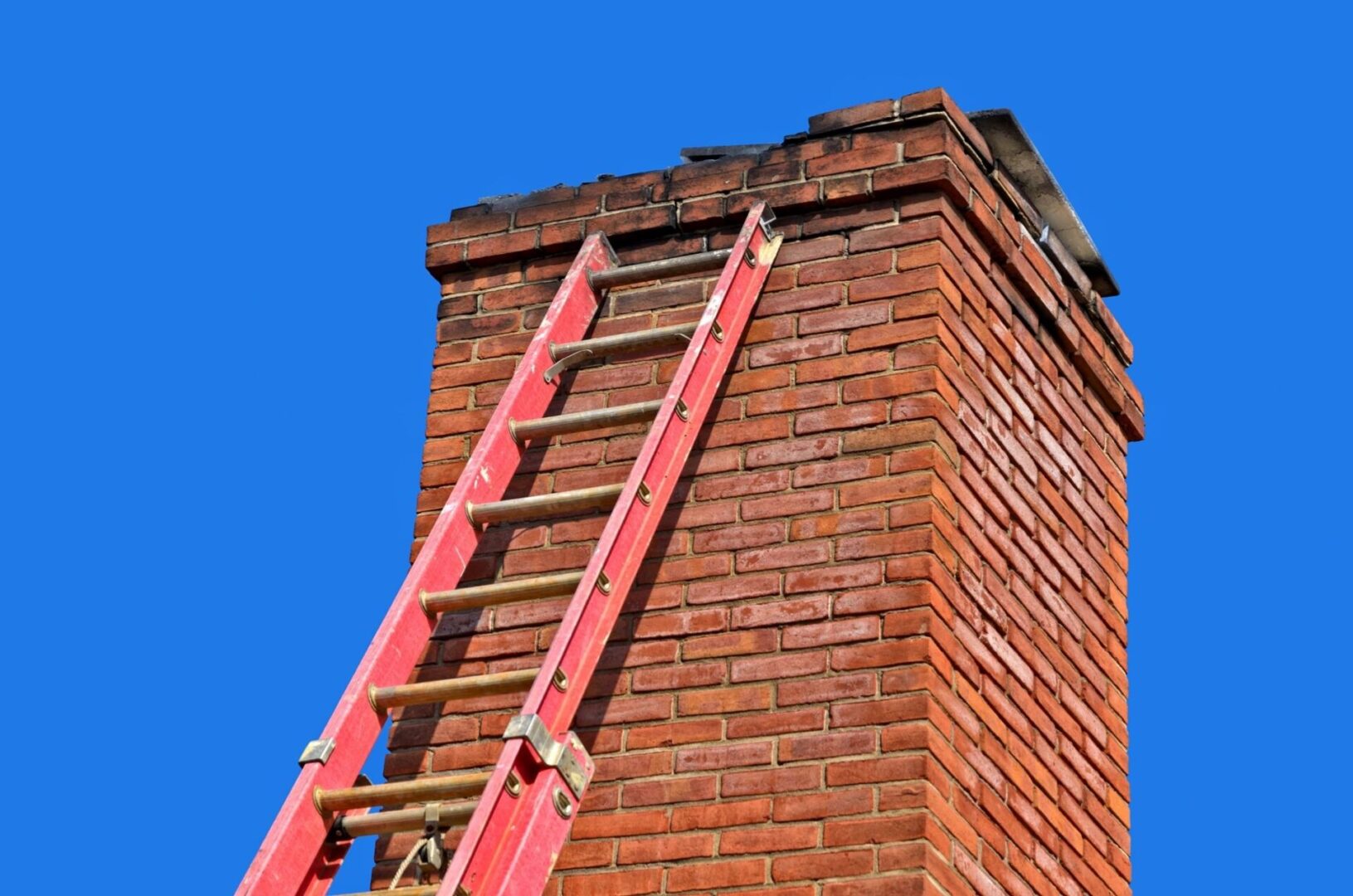 A ladder is on top of the brick chimney.